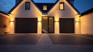 A two-story house with a central staircase, two garage doors, and exterior lighting.