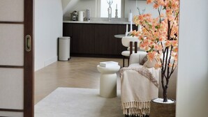 A modern interior with a wooden floor, a white sofa, a large potted plant, and a kitchen in the background.