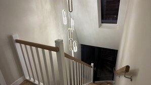 A staircase with a wooden handrail, a ceiling light fixture, and a window with blinds.