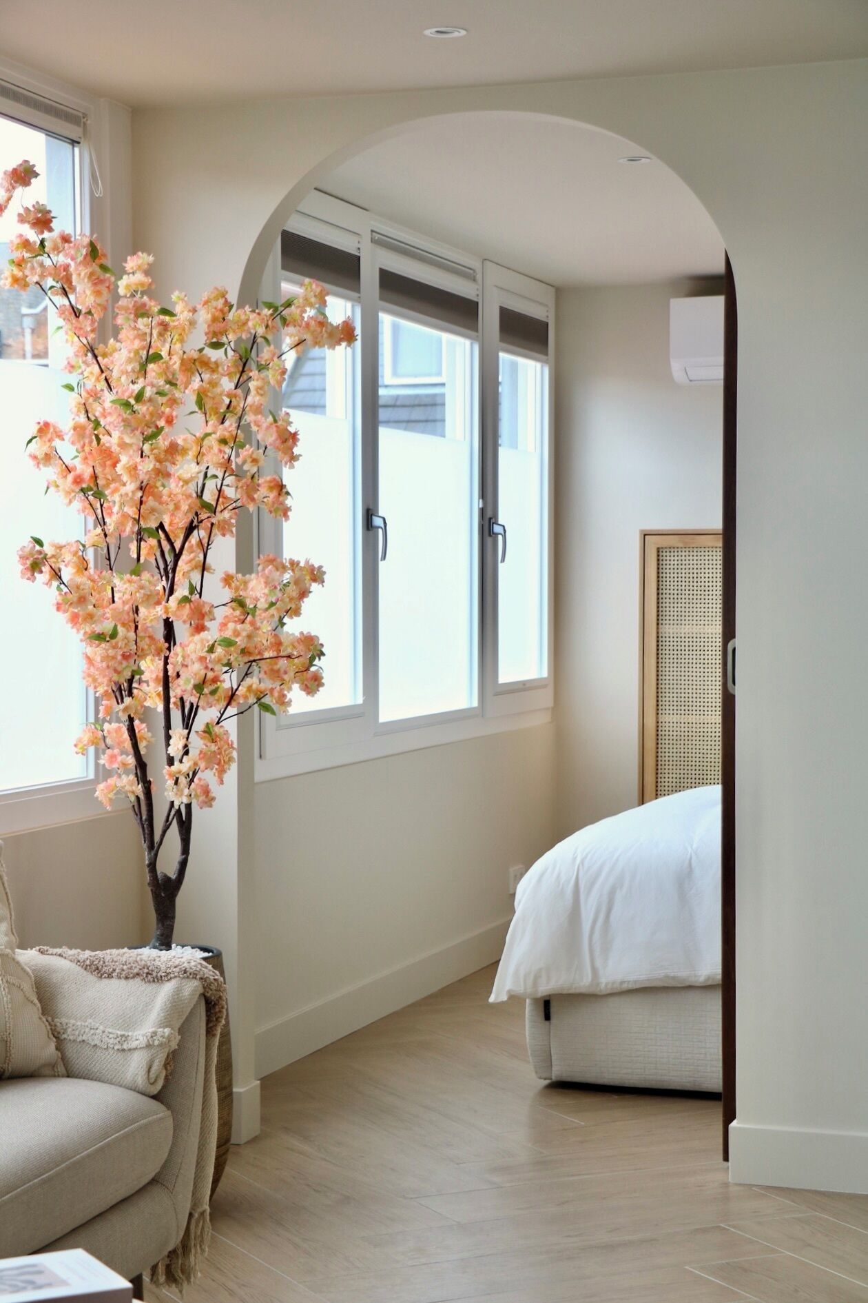 A bedroom with a bed, a window, and a decorative tree.