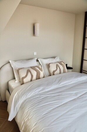 A bedroom with a bed, pillows, a nightstand, and a wall-mounted light fixture. - Breeze Inn - Japandi apartment - Strand, Leiden, Bioscience Park (Oegstgeest)