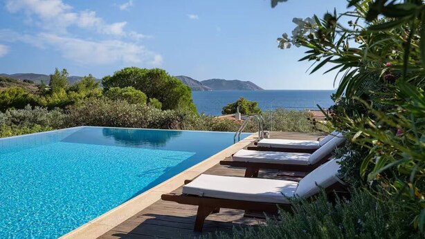 A clear blue pool with wooden deck and lounge chairs, surrounded by greenery and overlooking the sea. - Villa Valli Athenian Riviera, (Anavissos)