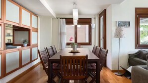 A dining area with a wooden table, chairs, a vase with flowers, and a pendant light. - Villa Valli Athenian Riviera, (Anavissos)