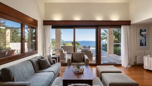 A spacious living room with a large sofa, a coffee table, and a view of the sea through large sliding glass doors. - Villa Valli Athenian Riviera, (Anavissos)