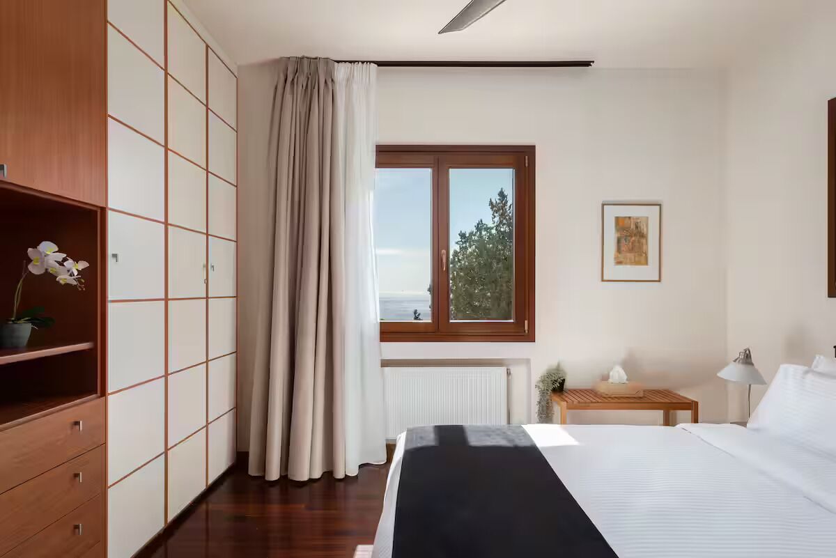 A hotel room with a bed, a window with a view, a radiator, a bedside table, and a wardrobe.