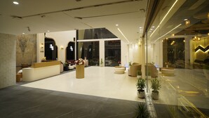 Een ruime lobby met een receptiebalie, zitgedeeltes en potplanten.