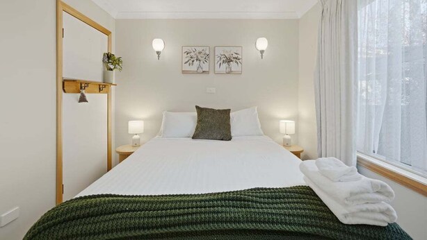 Een keurig ingerichte hotelkamer met een bed, bedlampjes, een spiegel en kunst aan de muur.