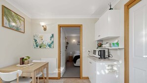 Een compacte keuken met een magnetron, een klein kastje en een eethoek met een tafel en stoelen.