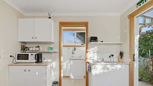 Een compacte keuken met witte kastjes, een magnetron, een spoelbak en een klein raam.