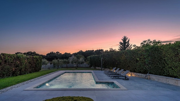 Una piscina rectangular con solárium pavimentado, rodeada de setos y árboles bien cuidados.