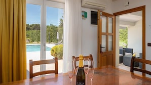 Una habitación con una mesa de comedor, sillas, una botella de champán y copas. Hay una puerta corrediza de vidrio que da a un área exterior con piscina y mobiliario.