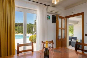 A room with a dining table, chairs, a bottle of champagne, and glasses. There is a sliding glass door leading to an outdoor area with a pool and furniture. - Villa Casa Rita (100601-K1) - Porec (Porec)