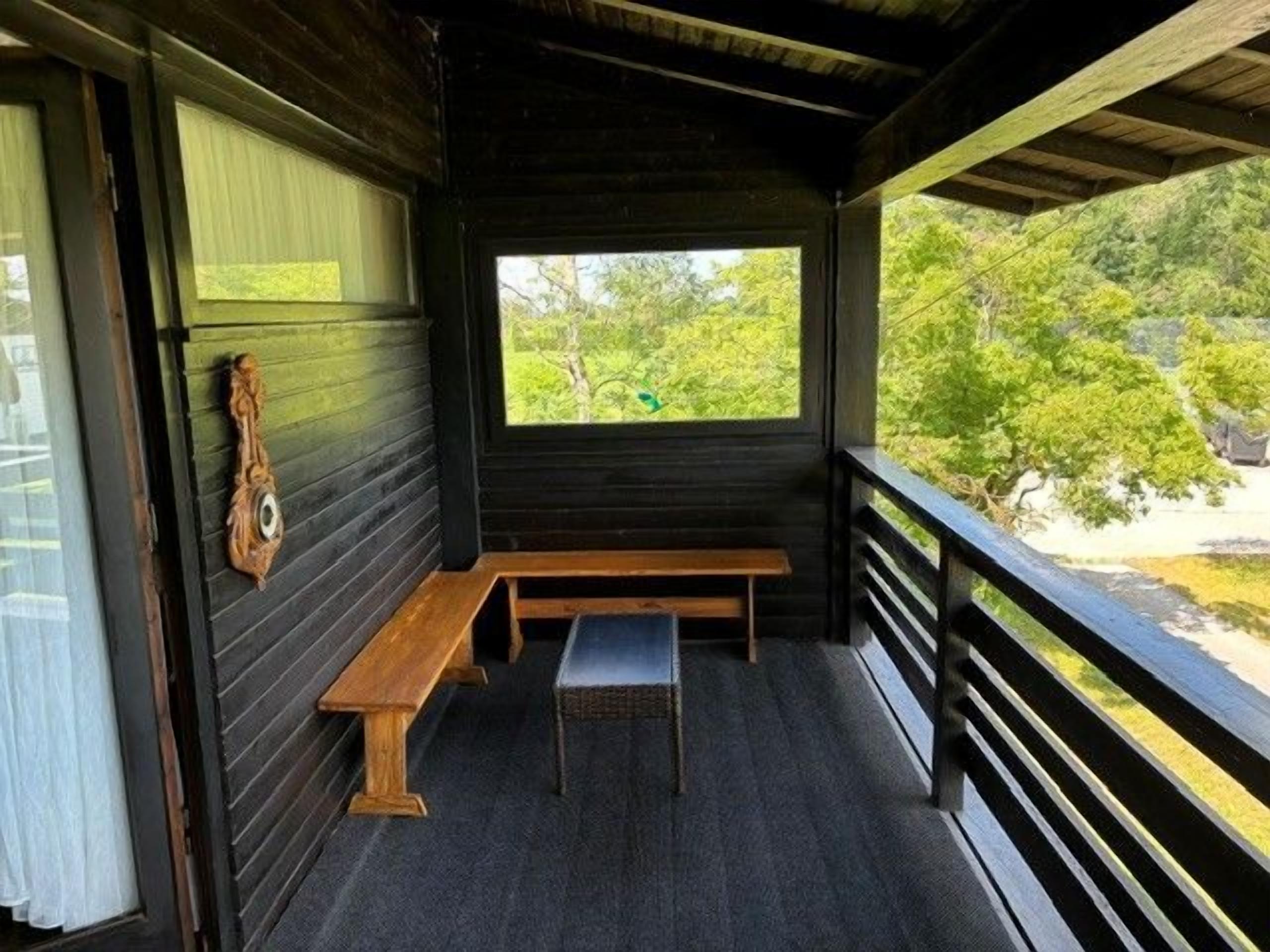 Eine hölzerne Bank und ein Fenster auf einer Veranda mit Blick auf Grünflächen.