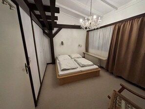 Un dormitorio con una cama, un candelabro, una ventana con cortinas y una puerta.