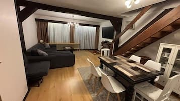 Una sala moderna con un sofá oscuro, una mesa de comedor con sillas y una escalera.