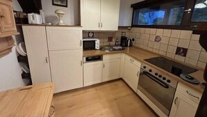 A compact kitchen with white cabinets, a microwave, a stove, and a wooden countertop. - Vacation apartment Knabenkraut 7 (Siegsdorf)
