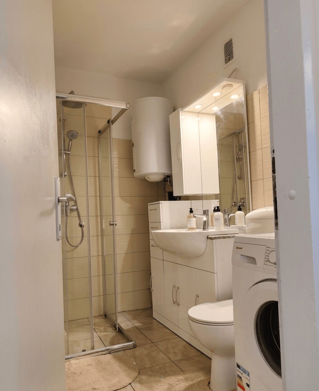 Un baño con ducha de vidrio, un lavamanos blanco, un inodoro y una lavadora.