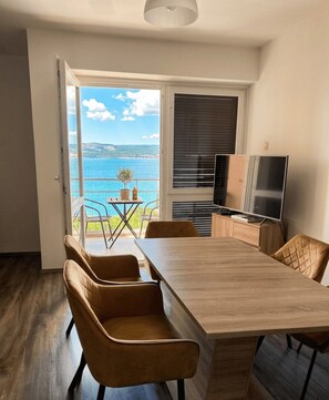 A modern kitchen with a wooden table, two chairs, a TV, and a balcony with a view of the sea. - Stylish 2-Bedroom Crikvenica Apartment with AC and Coastal Charm (Crikvenica)