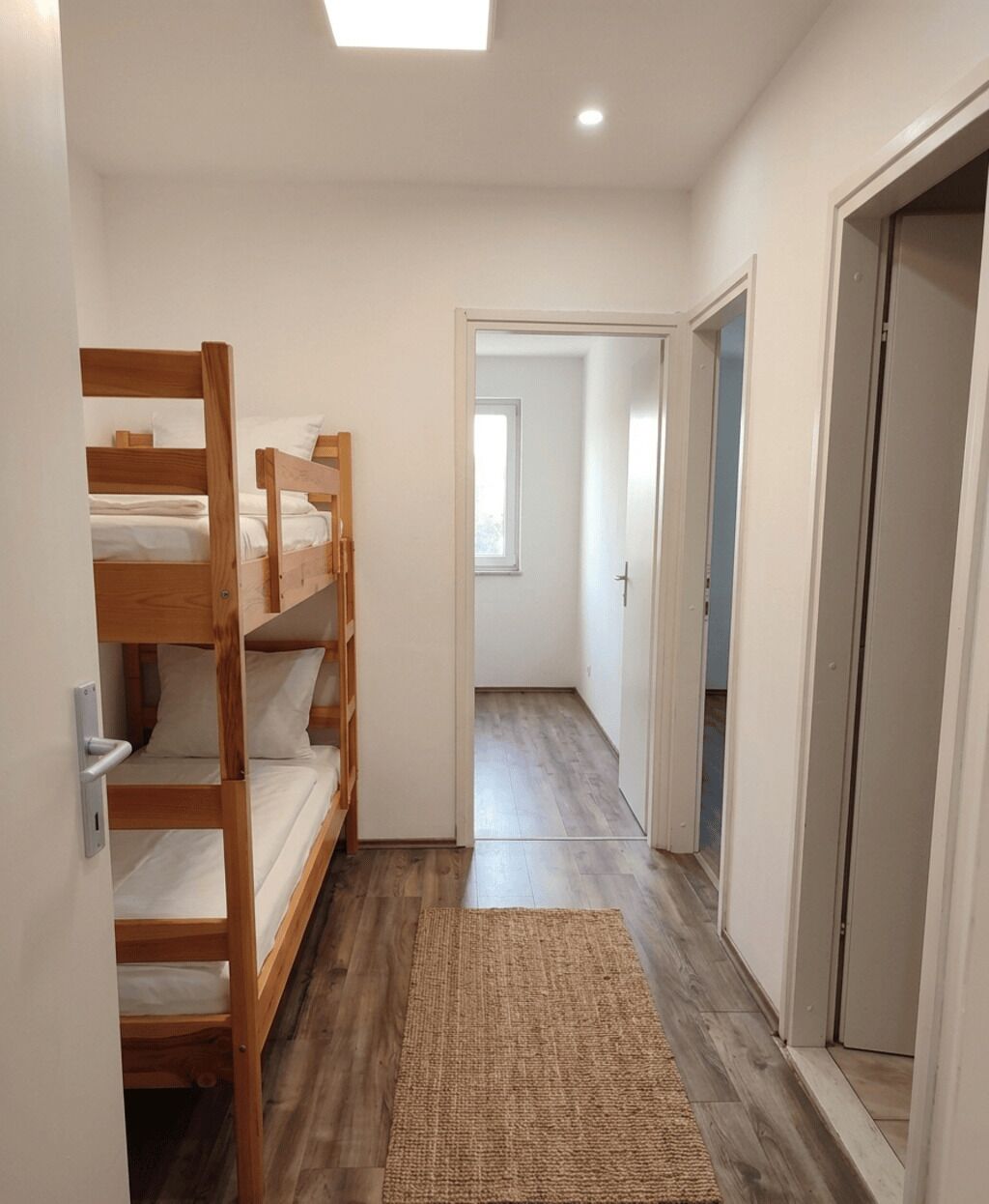 Un pasillo estrecho con literas a un lado y una puerta que da a otra habitación.