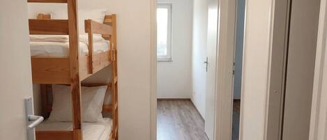 En smal hall med våningssängar på ena sidan och en dörr som leder till ett annat rum.