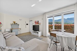 Ein modernes Wohnzimmer mit Sofa, Fernseher und Esstisch, große Fenster mit Blick auf die Berge.