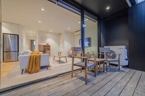 A modern living area with a sofa, coffee table, and chairs, a kitchen with a refrigerator, and an air conditioning unit. - Bright 2 Bedroom Apartment in Central Christchurch (Christchurch)