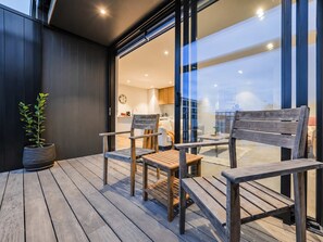 A deck with wooden furniture, a potted plant, and a view of an interior space. - Central City Stay | 2BR + Balcony | Parking (Christchurch)