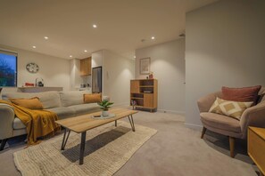 A living room with a sofa, a coffee table, a bookshelf, and a clock on the wall. - Bright 2 Bedroom Apartment in Central Christchurch (Christchurch)