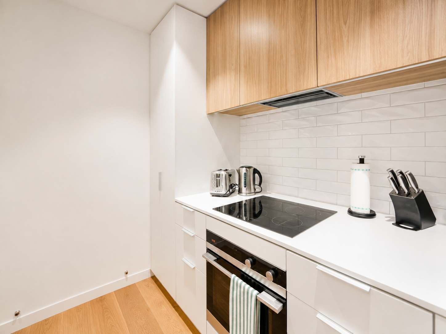 Una cocina moderna con armarios blancos, una placa de cocina por inducción negra, un hervidor, una cafetera y un bloque de cuchillos.