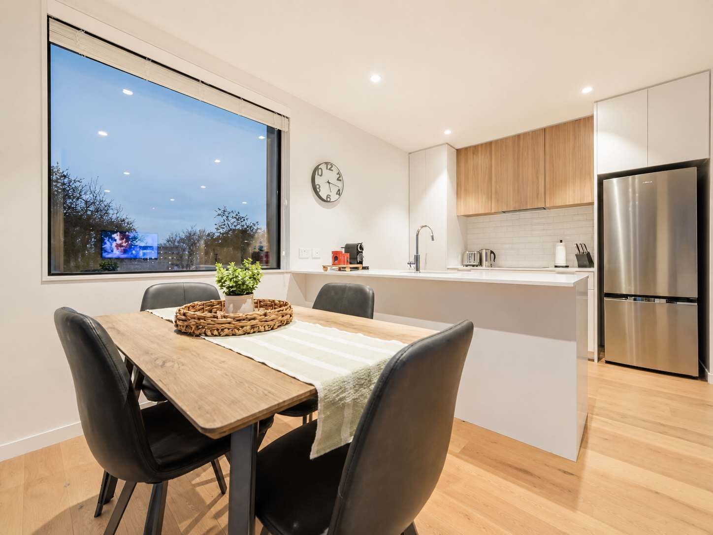 Una cocina moderna con un refrigerador de acero inoxidable, armarios de madera y un ventanal con vistas a un paisaje urbano.