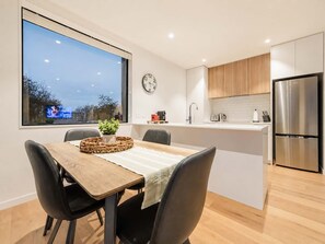 A modern kitchen with a stainless steel refrigerator, wooden cabinets, and a large window overlooking a cityscape. - Central City Stay | 2BR + Balcony | Parking (Christchurch)