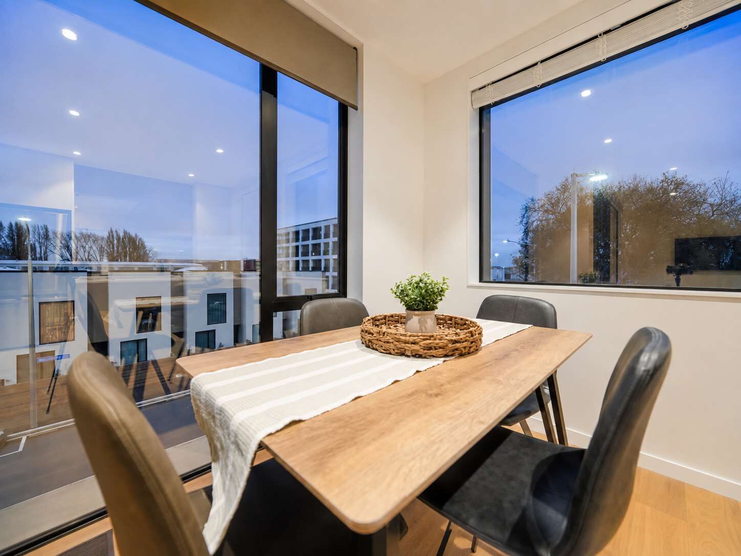 A dining area with a table, chairs, and a view through large windows.
