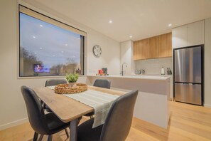 A modern kitchen with a dining area, a large window, and a stainless steel refrigerator. - Bright 2 Bedroom Apartment in Central Christchurch (Christchurch)