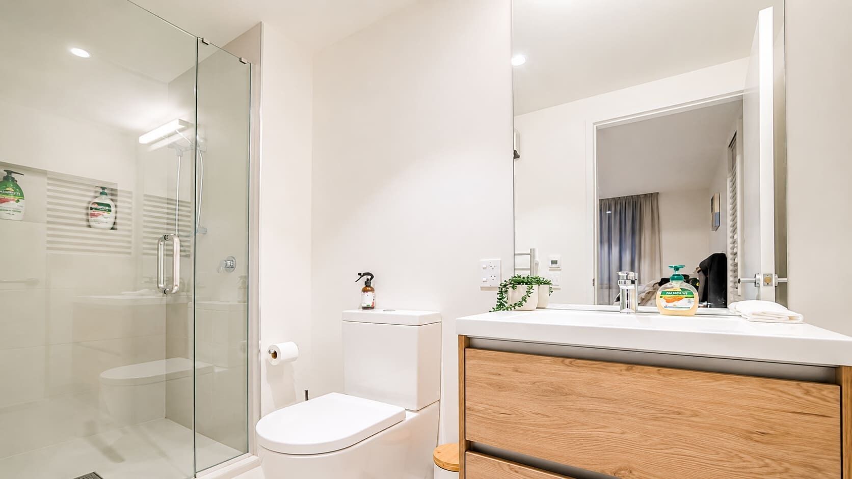 Un baño moderno con cabina de ducha de vidrio, inodoro, lavamanos con espejo y tocador de madera.