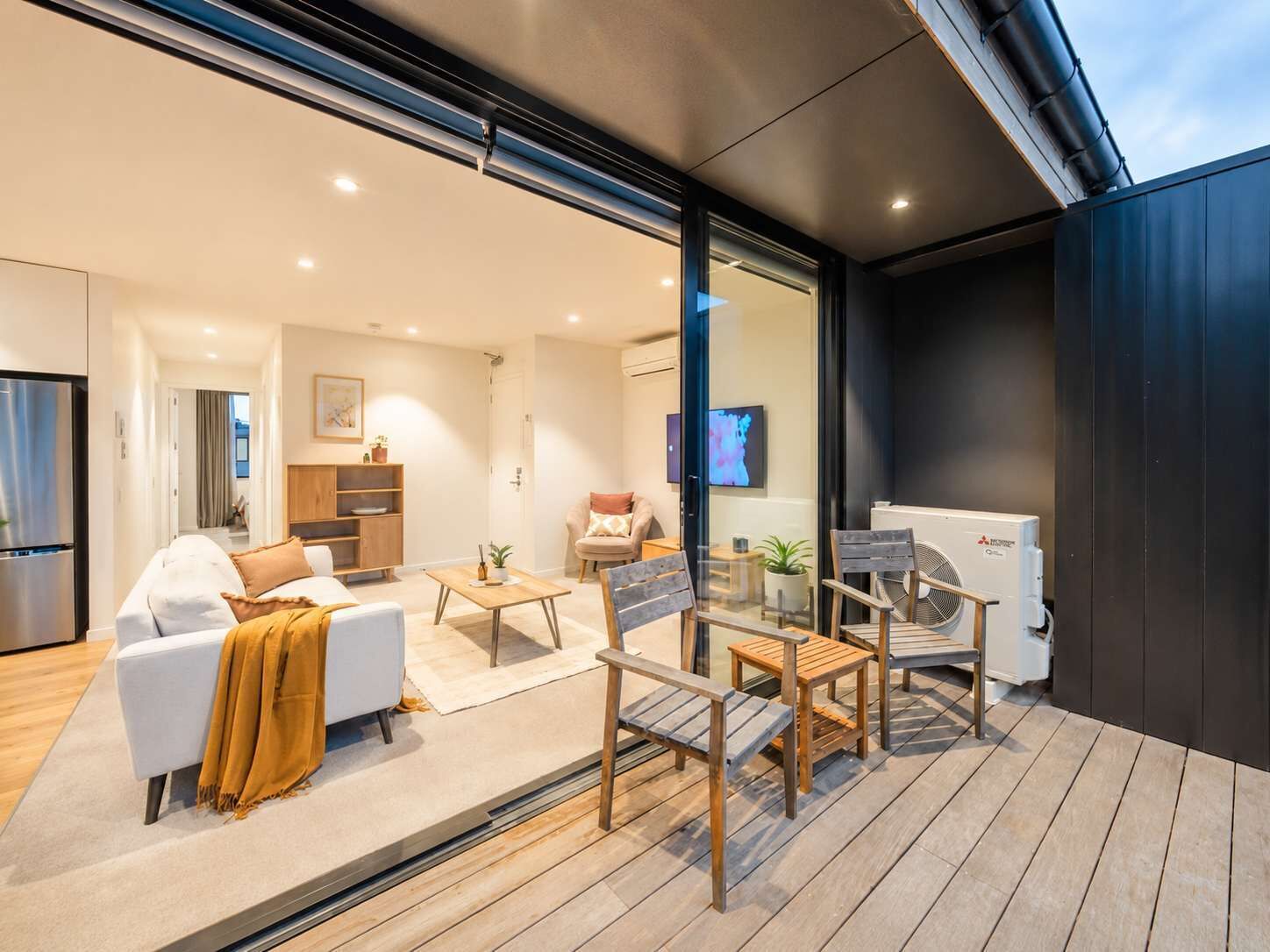 Ein modernes Wohnzimmer mit einer Couch, einem Couchtisch und Stühlen auf einer Holzterrasse.