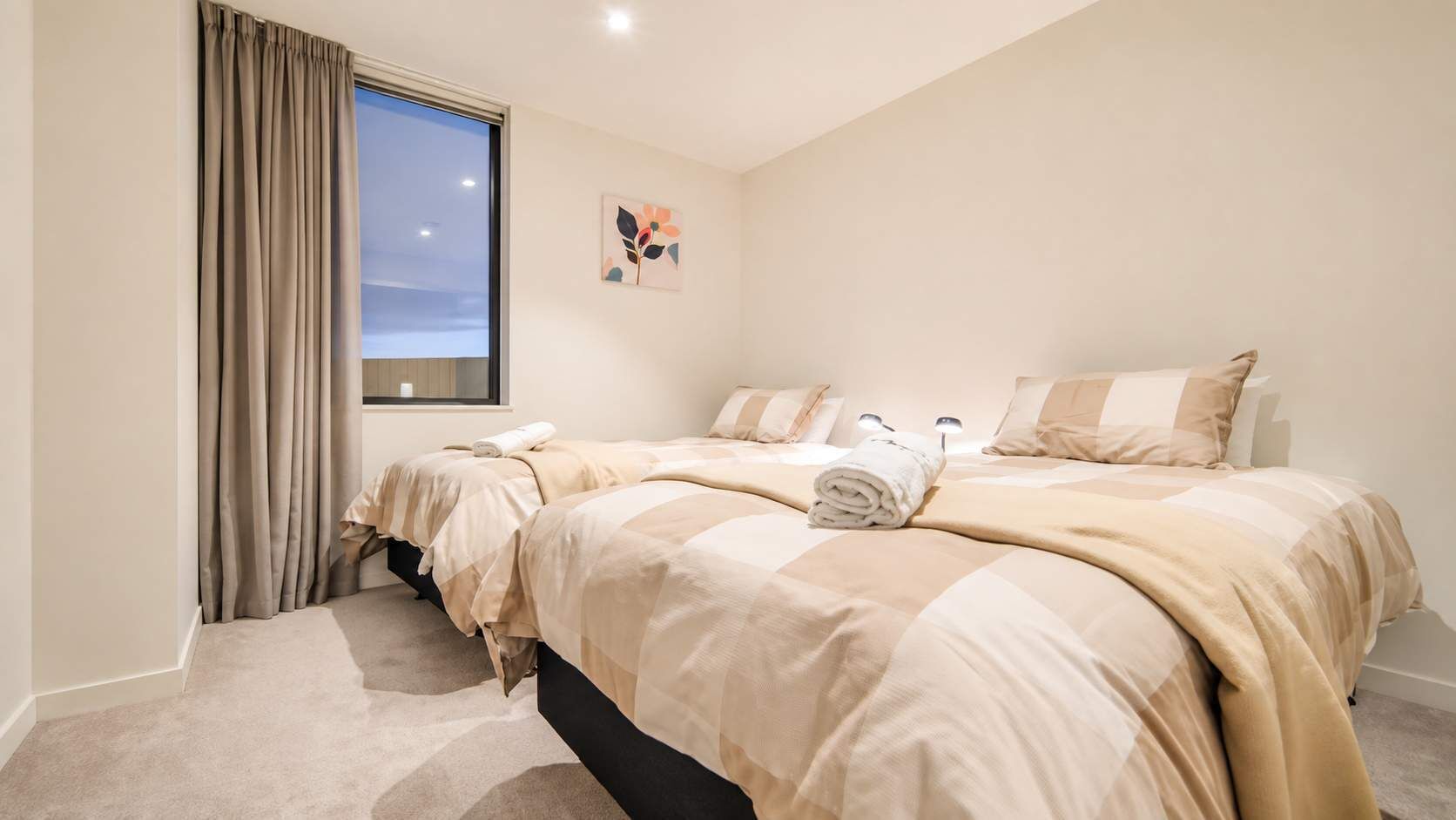 A hotel room with two beds, a window with curtains, a painting on the wall, and a carpeted floor.