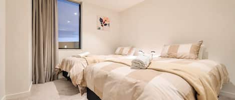 A hotel room with two beds, a window with curtains, a painting on the wall, and a carpeted floor.