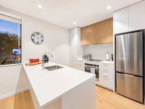 A modern kitchen with a central island, stainless steel appliances, and a wall-mounted clock. - Central City Stay | 2BR + Balcony | Parking (Christchurch)
