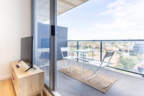 A balcony with a view of a cityscape, a TV on a wooden stand, and two white chairs. - South Yarra Retreat, Morning Hot Air Balloon Views (South Yarra)