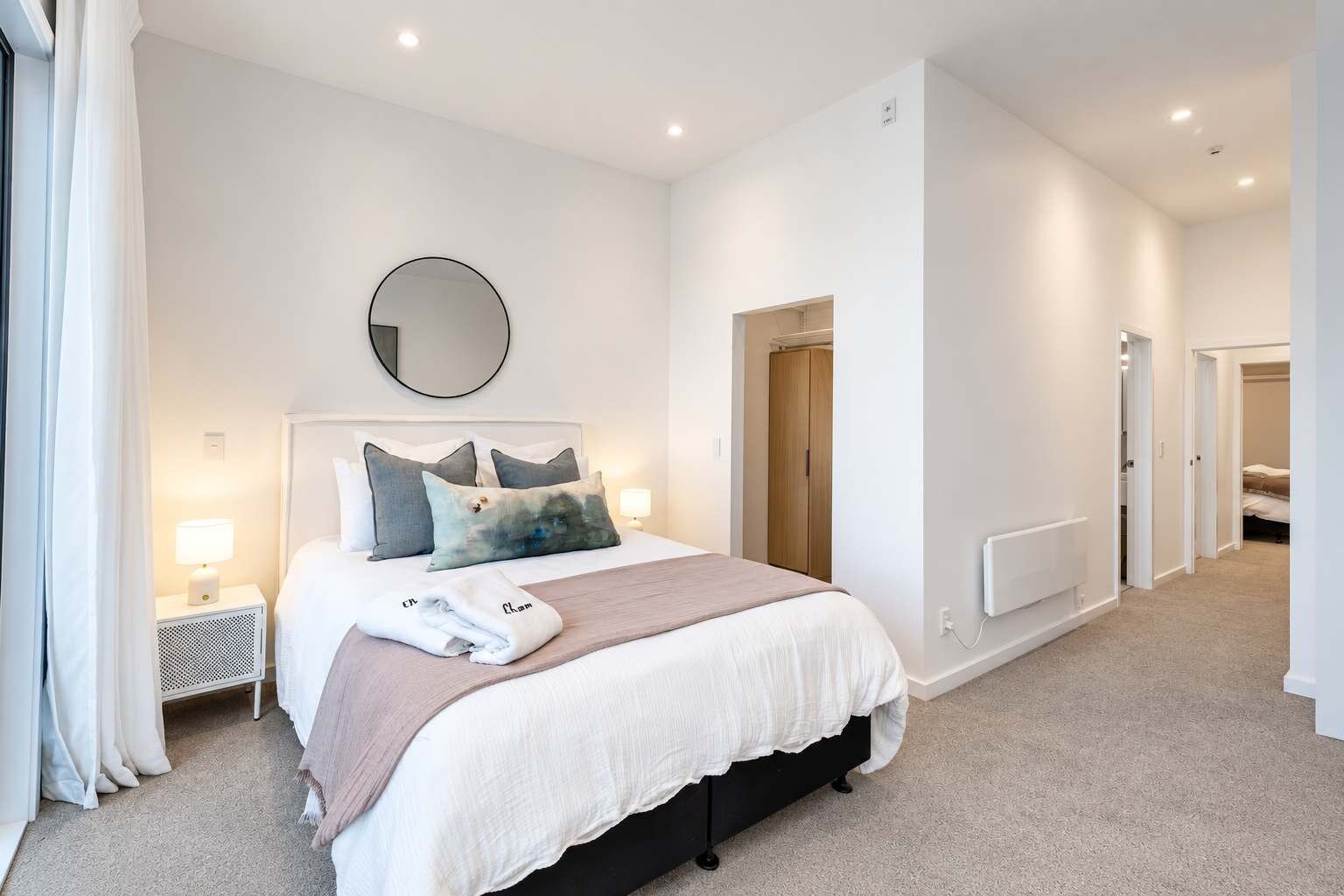 A modern bedroom with a bed, bedside lamps, a round mirror, and a wardrobe.
