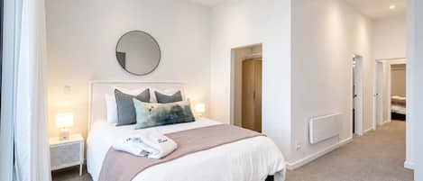 A modern bedroom with a bed, bedside lamps, a round mirror, and a wardrobe.