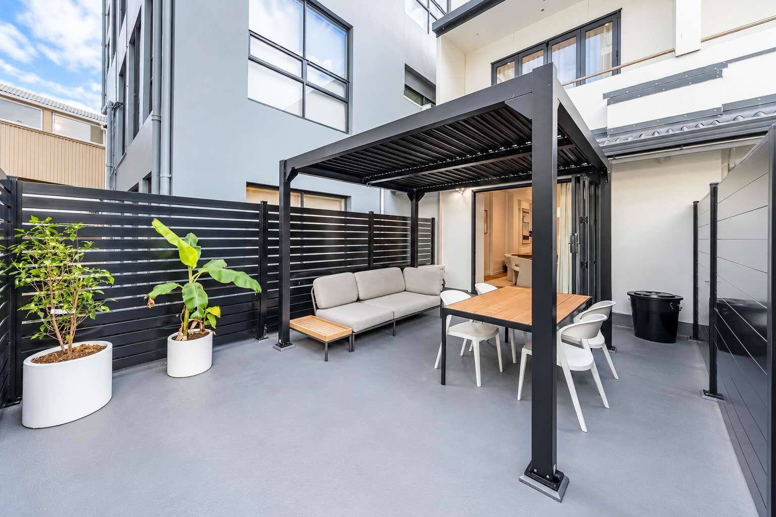A modern outdoor patio with a sofa, table, chairs, and potted plants.