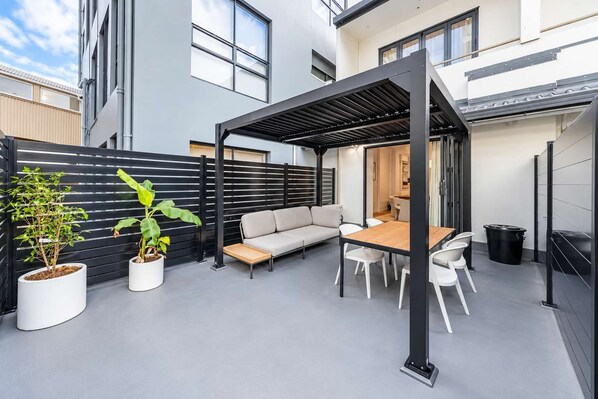 A modern outdoor patio with a sofa, table, chairs, and potted plants. - The Hudson | 3BR Bright Courtenay Place Townhouse (Wellington)