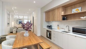 Une cuisine moderne avec des meubles blancs, une table à manger en bois et un four encastré.