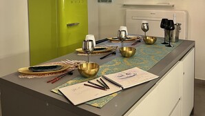 Una cocina con un refrigerador verde, una barra con vasos y una botella, y un televisor montado en la pared.