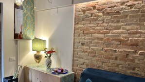 Una habitación con un sofá azul, una mesita con una lámpara y un florero, una pared de ladrillo y una puerta.