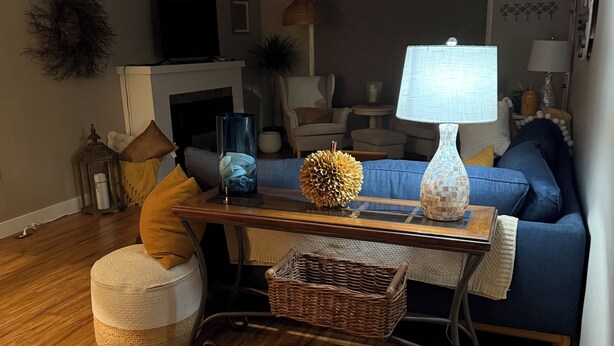 Uma sala de estar com sofá, pufê, mesa de centro, luminária e objetos decorativos.