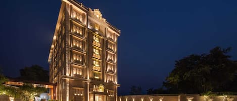 A multi-story hotel with a grand entrance, a well-lit facade, and a paved courtyard.