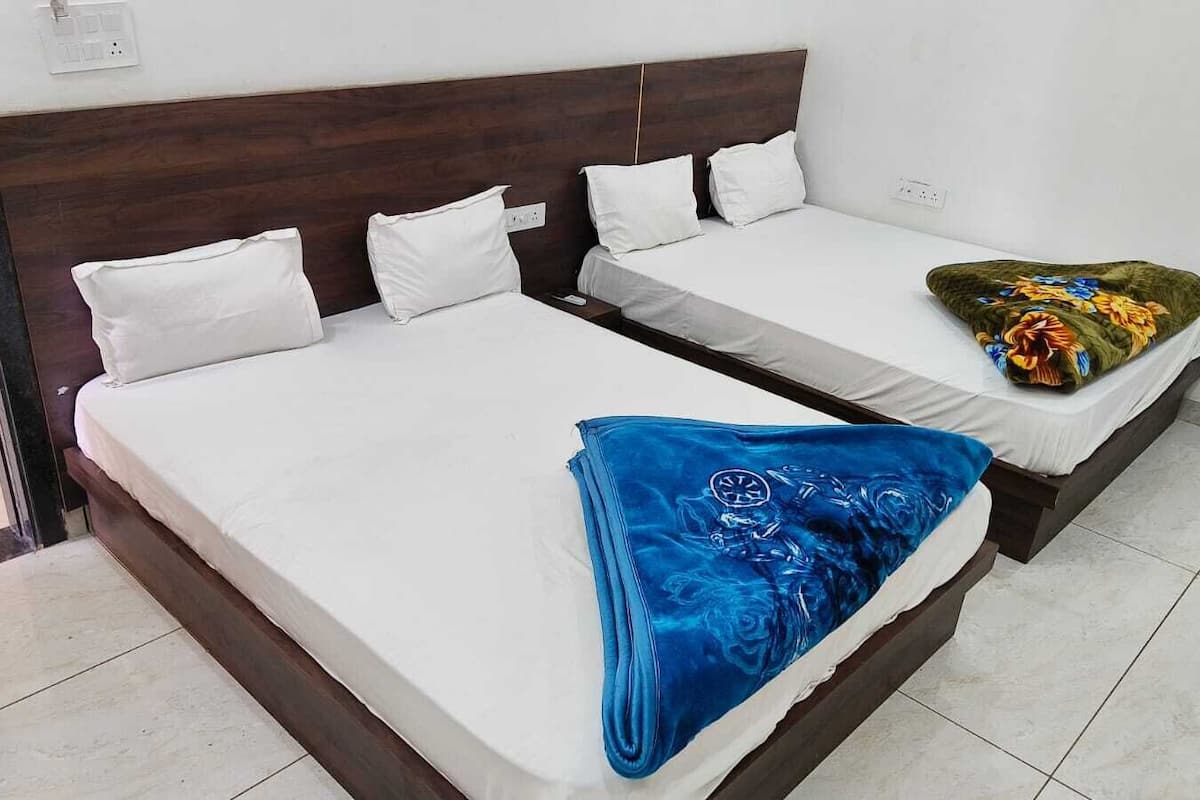 Habitación de hotel con dos camas, cabecero de madera, ropa de cama blanca y una manta azul sobre una de las camas.