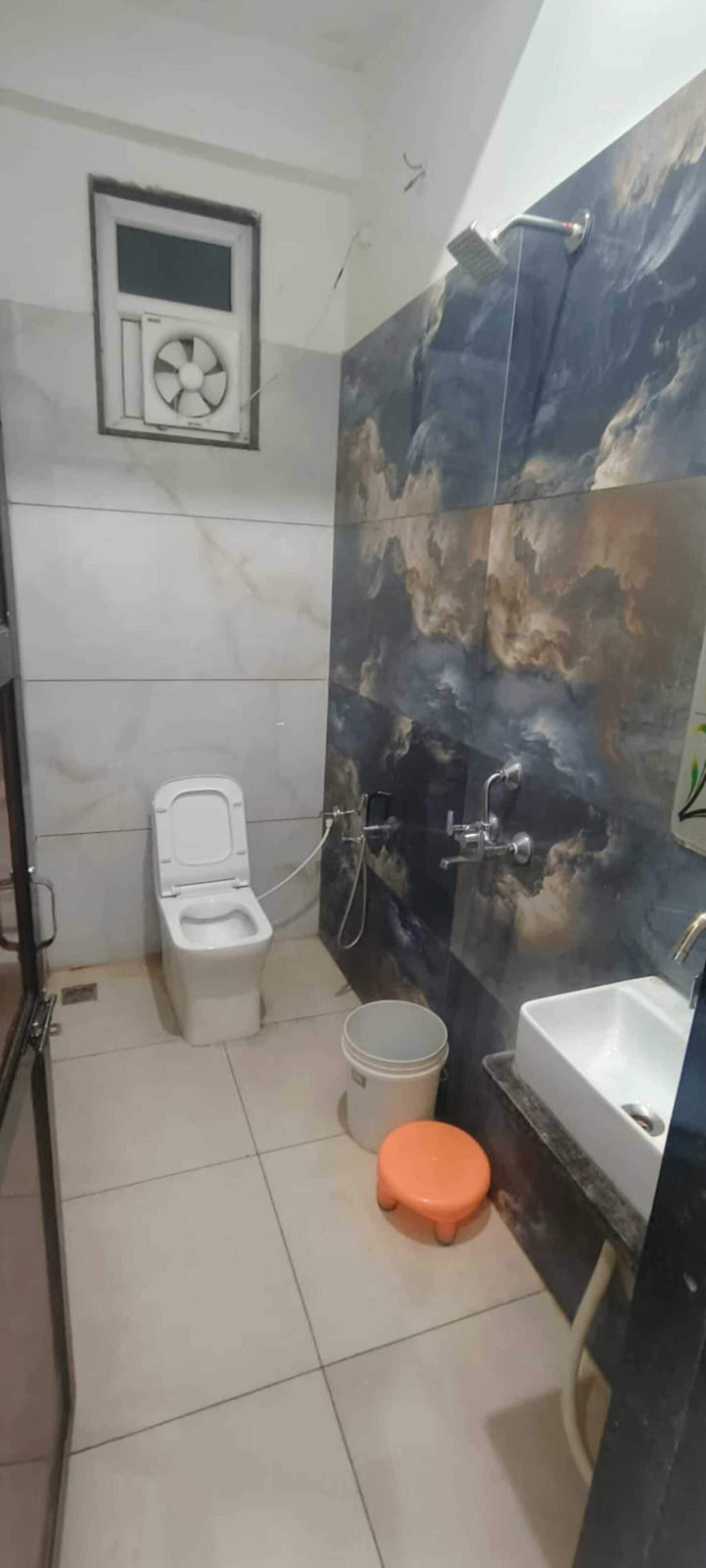 Un baño con inodoro, ducha, lavamanos y un ventilador en la pared.